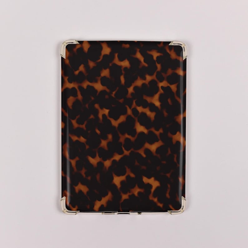 May include: A rectangular case with a tortoiseshell pattern in shades of brown and black. The corners are reinforced with silver-colored metal. The case is likely designed to hold a tablet or similar electronic device.