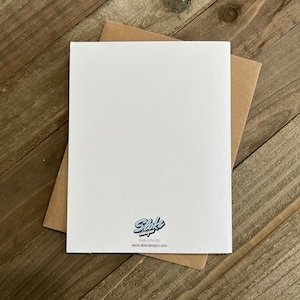 May include: Blank white card with a brown envelope. The card has a small logo in the bottom right corner that says "Sloke Designs" and "made in the USA" with the website "www.slokedesigns.com" below the logo.