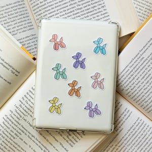 May include: A clear phone case with colorful balloon dog stickers in various colors, including pink, blue, green, yellow, and orange.