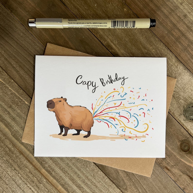 May include: A white greeting card with a cartoon capybara with colorful confetti coming out of its rear end. The card says "Capy Birthday".