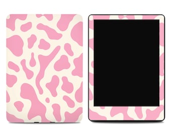 May include: A rectangular electronic tablet device featuring a protective skin with a repeating pink and cream cow print pattern. The device is shown from both the front, displaying a black screen, and the back, showing the full patterned surface.