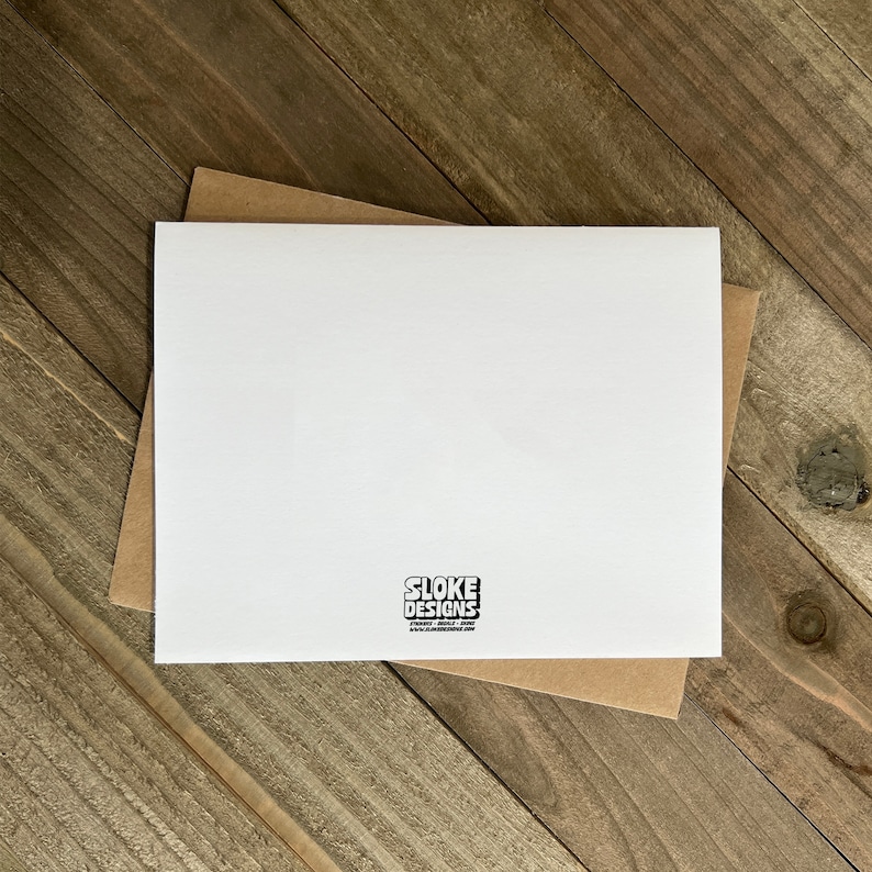 May include: Blank white card with a brown envelope. The card has a small black logo that says "Sloke Designs" with a website address.