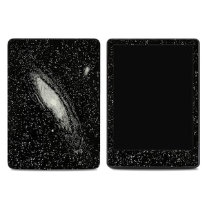 May include: A black e-reader with a galaxy design on the back cover. The design features a white and gray spiral galaxy against a black background with white star-like specks. The screen is black.