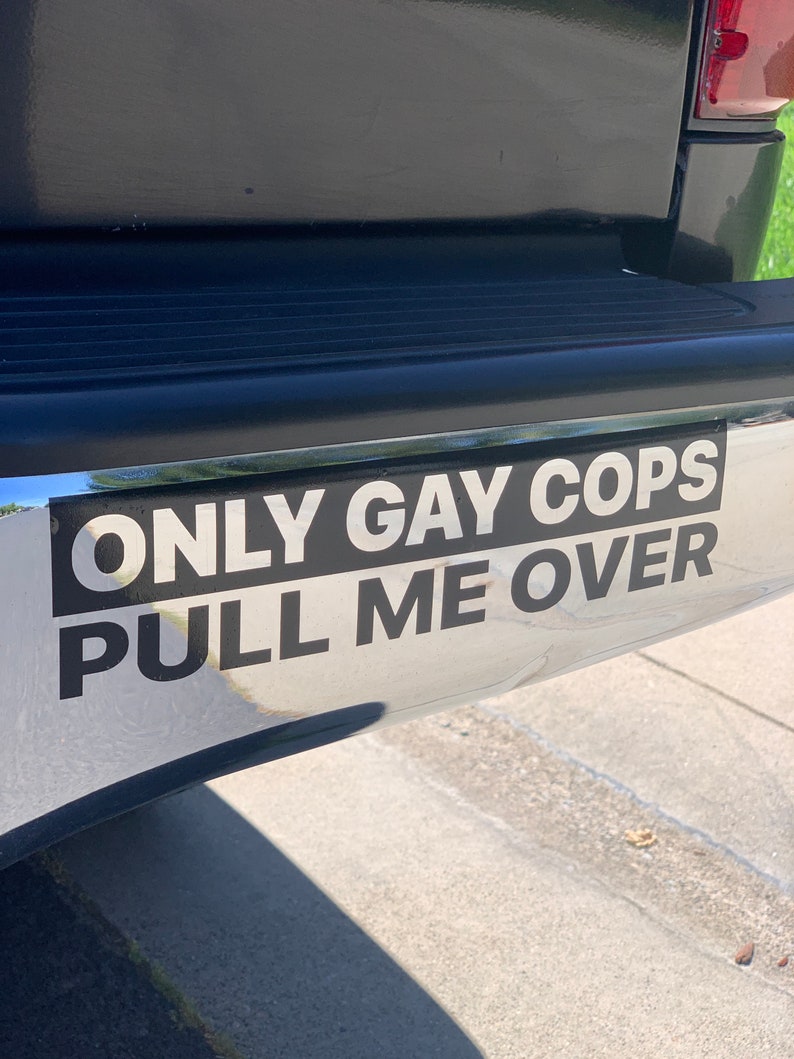 Puede incluir: Una pegatina negra en un parachoques plateado de una camioneta negra dice "ONLY GAY COPS PULL ME OVER".