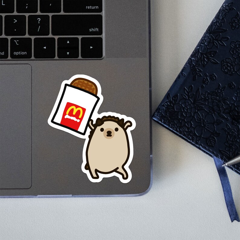 May include: A sticker of a cartoon hedgehog holding a McDonald's McChicken sandwich. The hedgehog is brown with a white belly and has a brown nose and eyes. The McChicken sandwich is in a white paper wrapper with the McDonald's logo in red and yellow.