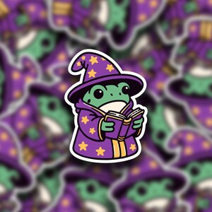 May include: A green frog wearing a purple wizard hat with yellow stars and a purple robe, holding a closed purple book.