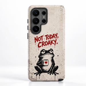 Könnte beinhalten: Eine Smartphone-Hülle mit strukturiertem beigen Hintergrund und einer schwarzen Grafik eines Frosches, der eine kleine weiße Tasse mit einem roten Herz hält. Darüber steht der Text "NOT TODAY, CROAKY." in roter, tropfender Schrift.