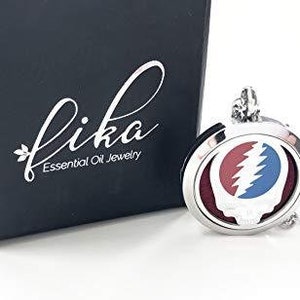 May include: A silver essential oil diffuser necklace with a Grateful Dead skull and lightning bolt design. The necklace is on a silver chain and comes in a black box with the word "fika" and "Essential Oil Jewelry" printed on it.