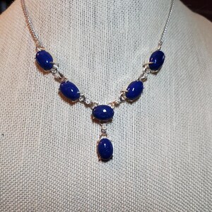 May include: A silver necklace with a pendant and five oval-shaped blue stones.