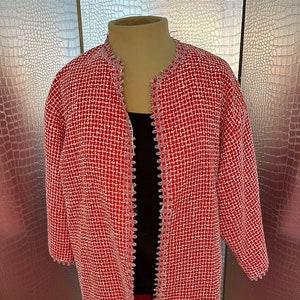 May include: A red and white tweed jacket with a scalloped trim. The jacket has a long, open front and three-quarter sleeves.