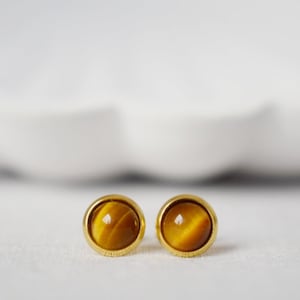 Könnte beinhalten: Ein Paar goldene Ohrstecker mit runden Tigeraugen-Steinen.