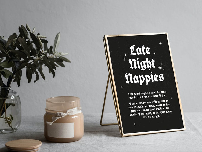 May include: A black framed sign with white text that reads "Late Night Nappies". The sign has a gold frame and is sitting on a table with a candle and a plant.
