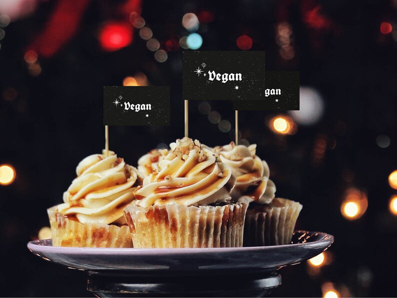 May include: Three vegan cupcakes with caramel frosting and pecan toppings, decorated with black flags that say "vegan" in white lettering.
