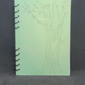 Peut inclure: Un carnet à spirales vert avec un dessin au trait noir et blanc d'un arbre avec une forme de cœur dans le tronc.