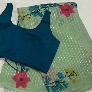 May include: A teal blue sleeveless blouse with a green and white saree with floral print and sequins.