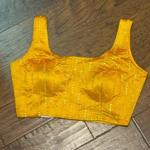 May include: A yellow sleeveless blouse with a scoop neck and sequins. The blouse has a fitted bodice and a straight hem.