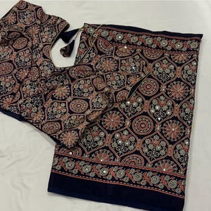 May include: A dark navy blue fabric garment featuring an intricate repeating pattern of floral motifs and geometric shapes in shades of orange, white, and light blue. The design is accented with small, reflective circular mirror embellishments.