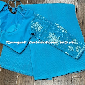 May include: A turquoise blue pleated saree with a matching turquoise blue blouse featuring a white embroidered design. The blouse has long sleeves with a decorative pattern.