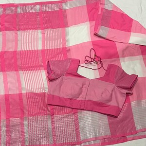 May include: A pink and white checkered saree with a matching pink blouse. The saree has a silver thread woven into the fabric.