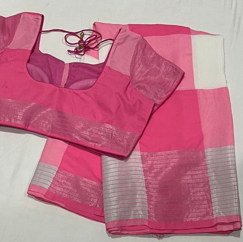 May include: A pink and white checkered saree with a silver border. The saree comes with a matching pink blouse.