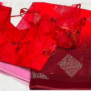 May include: A red and pink saree with a sequined design. The saree has a matching red blouse with a floral pattern.