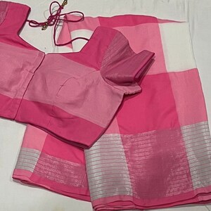 May include: A pink and white checkered saree with a silver border. The saree is paired with a pink blouse with a matching checkered pattern.