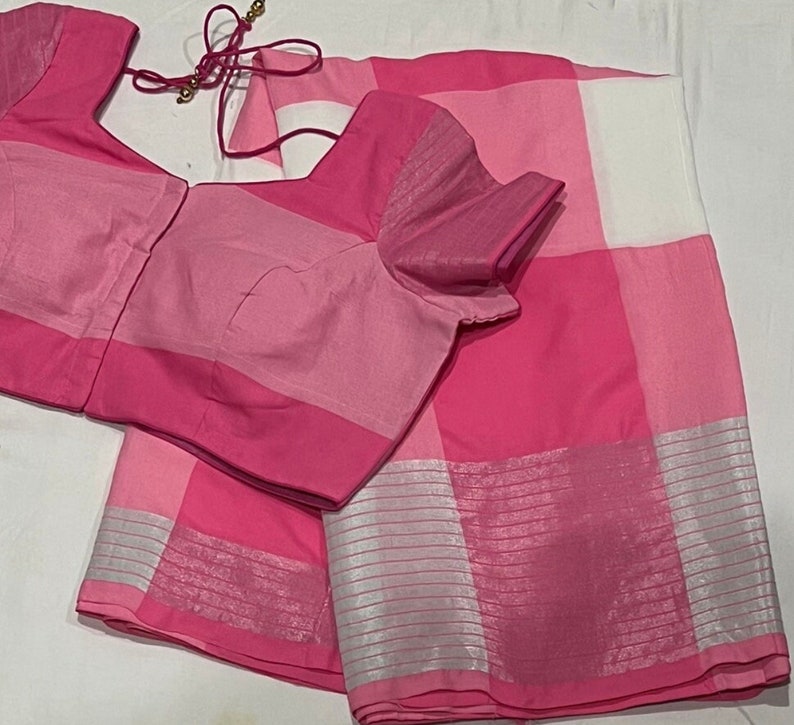 May include: A pink and white checkered saree with a silver border. The saree is paired with a pink blouse with a matching checkered pattern.