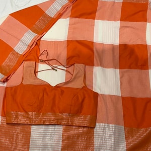 May include: A white and orange checkered saree with a matching orange blouse. The saree has a silver border and the blouse has a silver trim.