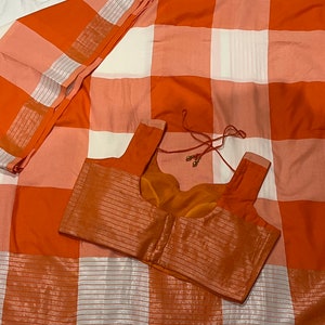 May include: Orange and white checkered saree with a matching orange blouse. The saree has a silver thread design.