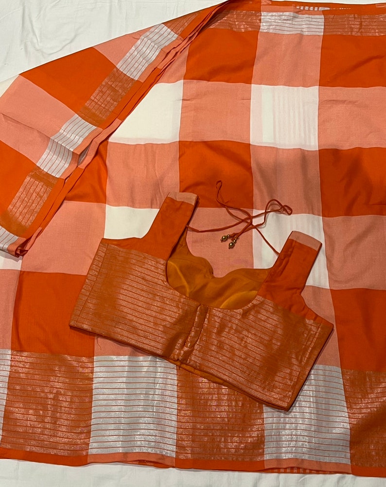 May include: Orange and white checkered saree with a matching orange blouse. The saree has a silver thread design.