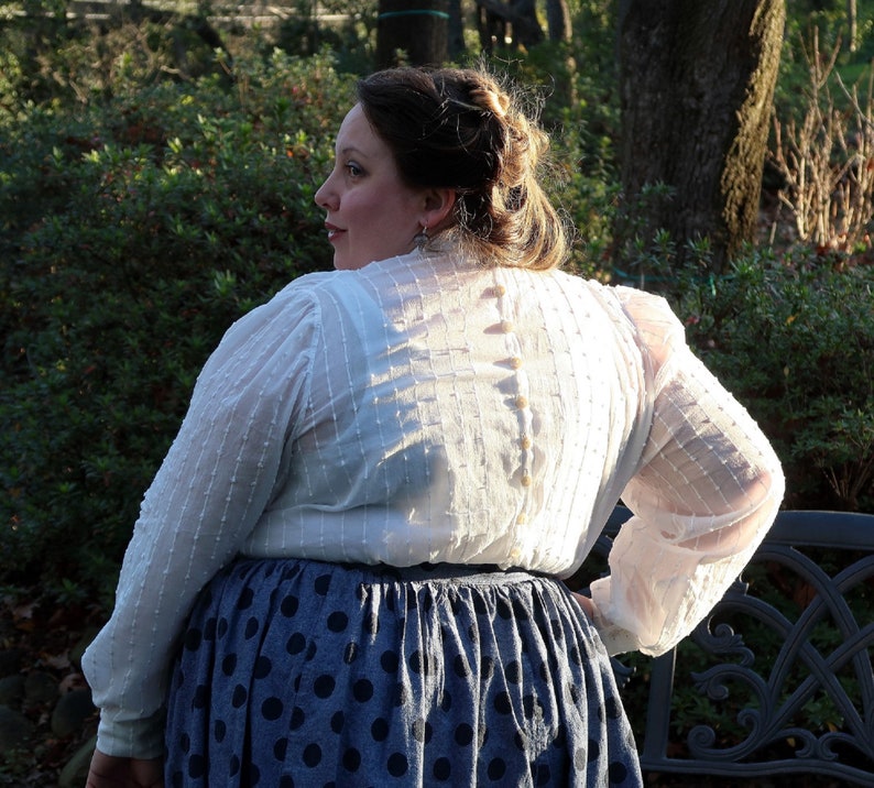 May include: A white, sheer blouse with a button-up back and a polka dot skirt. The blouse has a textured, almost quilted look.