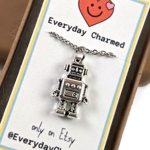 May include: A silver robot charm necklace in a small box with a white card that says "Everyday Charmed" and a red heart with a pink heart on top. The card also says "only on Etsy @EverydayCharmed".