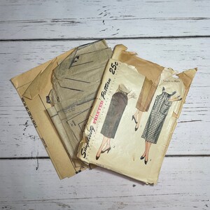 May include: Vintage Simplicity sewing patterns, featuring illustrations of skirts and dresses. The patterns are in worn paper envelopes, with the price of 25 cents printed on the front. The background is a white wooden surface.