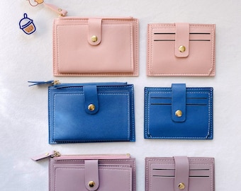 Pode incluir: Seis carteiras pequenas em três cores: rosa, azul e roxo. Cada carteira tem um fecho de correr, uma aba com fecho de botão e um slot para cartões.