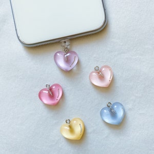 May include: Five heart-shaped charms in different pastel colours: light blue, pink, yellow, and two shades of pink. The charms have a silver loop at the top and are made of a translucent material.