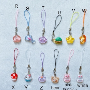 Pode incluir: Um conjunto de 12 pingentes de animais coloridos com cord&otilde;es de diferentes cores. Os pingentes incluem um polvo rosa, um golfinho azul, uma nuvem roxa, uma tartaruga verde, uma estrela amarela, um cavalo-marinho laranja, um cogumelo vermelho, um cupcake azul, um gato roxo, um urso castanho, um coelho rosa e um coelho branco.