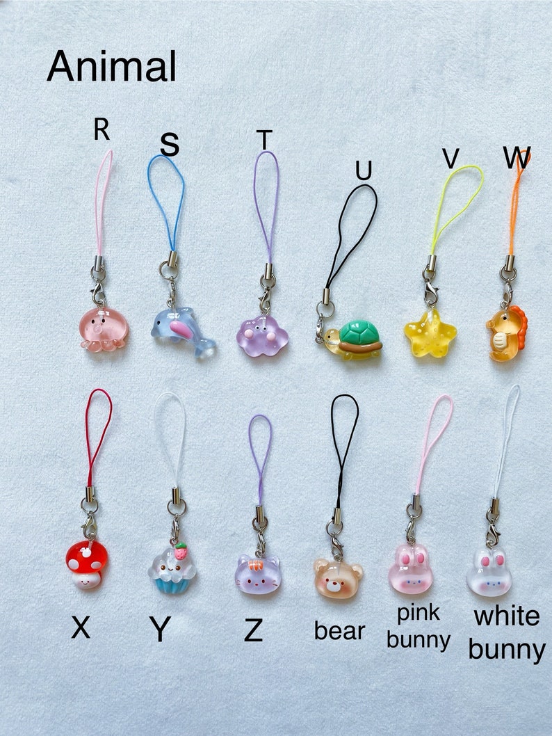 Pode incluir: Um conjunto de 12 pingentes de animais coloridos com cord&otilde;es de diferentes cores. Os pingentes incluem um polvo rosa, um golfinho azul, uma nuvem roxa, uma tartaruga verde, uma estrela amarela, um cavalo-marinho laranja, um cogumelo vermelho, um cupcake azul, um gato roxo, um urso castanho, um coelho rosa e um coelho branco.