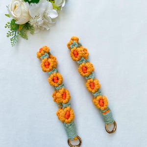May include: Two crocheted straps with a floral design in shades of orange and green. Each strap has a gold metal clasp.