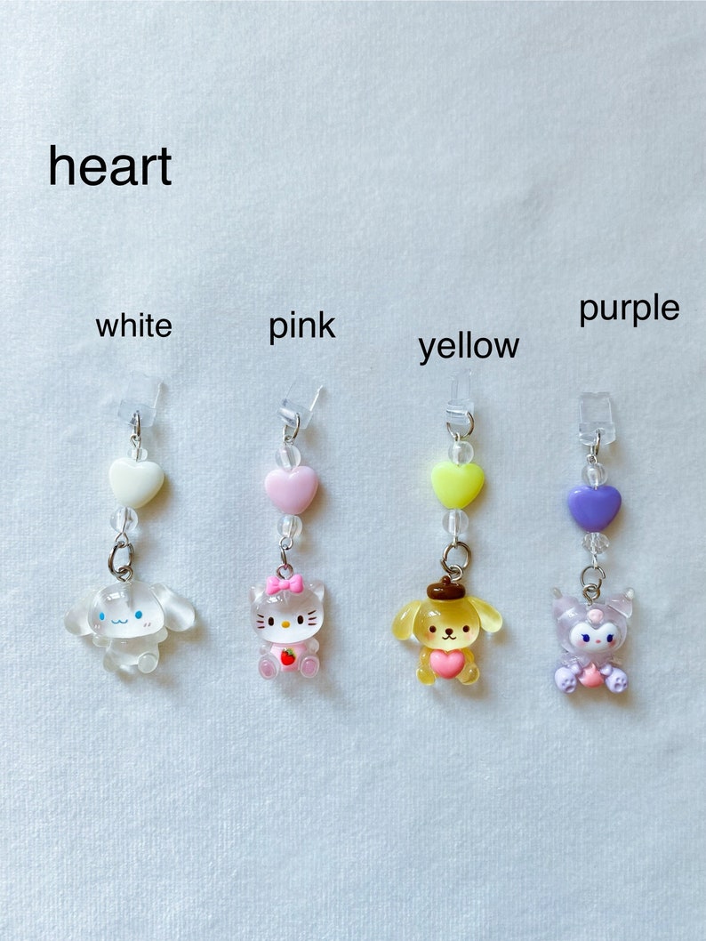 May include: Four heart-shaped charms with different characters on them. The charms are white, pink, yellow, and purple. Each charm has a small heart bead and a clear bead above it. The characters are a white dog, a pink cat, a yellow dog, and a purple cat.