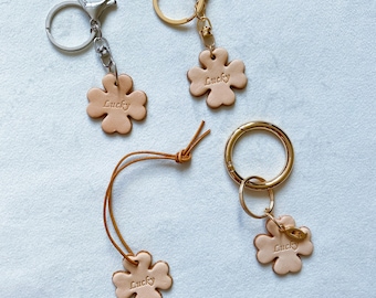 May include: Three leather keychains with four-leaf clover charms. Each charm has the word "Lucky" engraved on it. The keychains are attached to different types of rings: a silver split ring, a gold split ring, and a gold round ring.