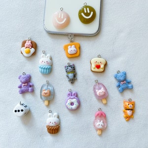 May include: A collection of 15 colorful charm pendants featuring various cute cartoon characters and designs, including a donut, a bear, a cat, a bunny, a dice, and a popsicle. The charms are made of polymer clay and have a hole for attaching to a keychain or necklace.