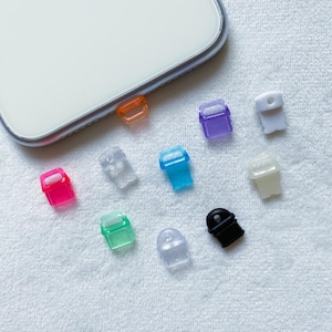 May include: Assortment of colorful phone charms in various shapes and colors, including clear, pink, blue, green, orange, white, and black. The charms are made of plastic and have a small hole at the top for attaching to a phone case.
