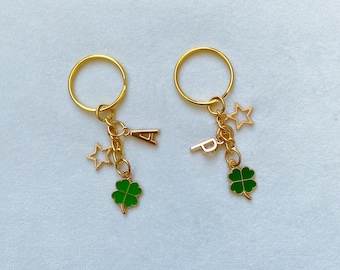 May include: Two gold keychains with green four-leaf clover charms, gold star charms, and letter charms. One keychain has the letter "A" and the other has the letter "P".