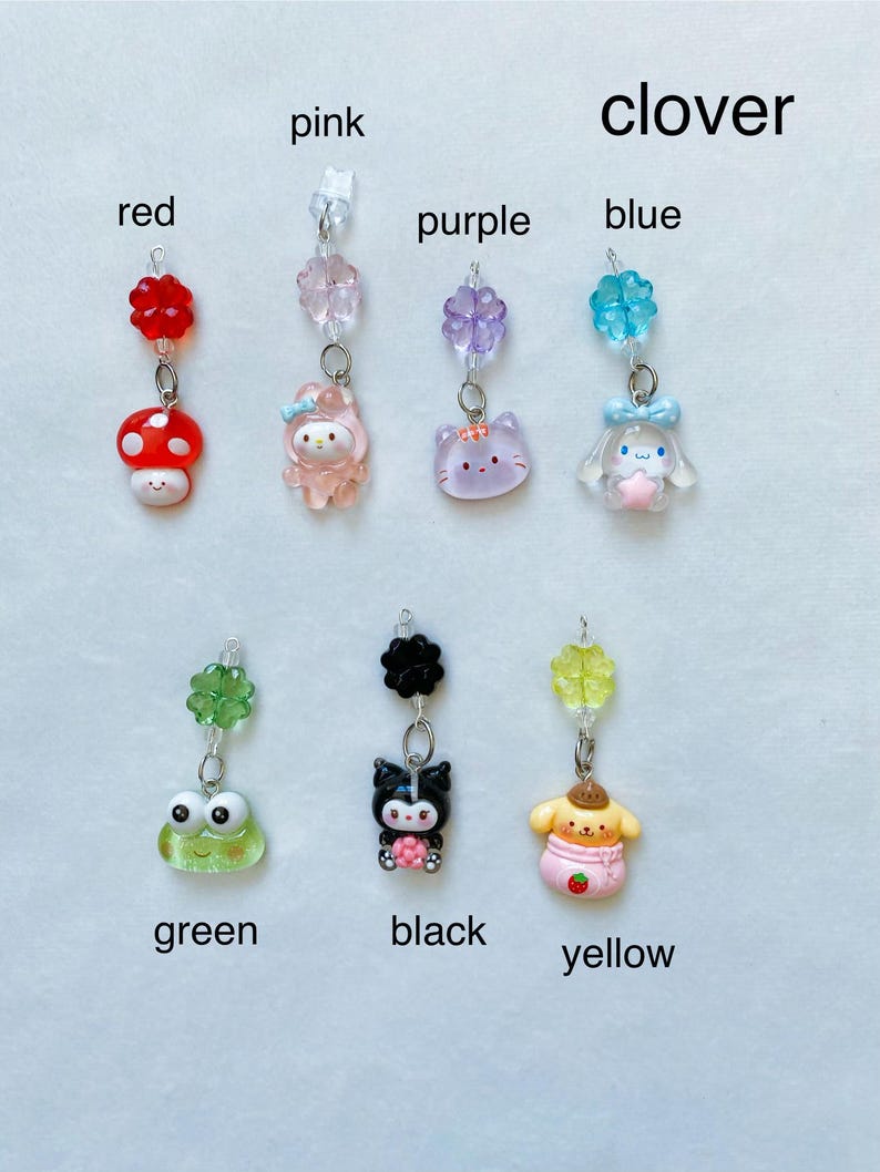 May include: A set of 10 charm pendants featuring various colours and characters. The charms are attached to a clear string and include a red mushroom, a pink Hello Kitty, a purple cat, a blue clover, a green frog, a black Kuromi, a yellow Pompompurin, a pink flower, a purple flower, and a blue flower.