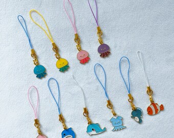 May include: A collection of colorful sea creature charms, including jellyfish, dolphins, and fish. Each charm is attached to a gold-colored clasp and a matching colored cord. The charms are in various colors, such as pink, blue, yellow, and purple.