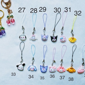 Pode incluir: Um conjunto de 12 pingentes de telefone coloridos com v&aacute;rios personagens de desenhos animados. Os pingentes s&atilde;o presos a cordas de diferentes cores, incluindo preto, branco, azul, rosa e amarelo. Os pingentes s&atilde;o numerados de 27 a 39.