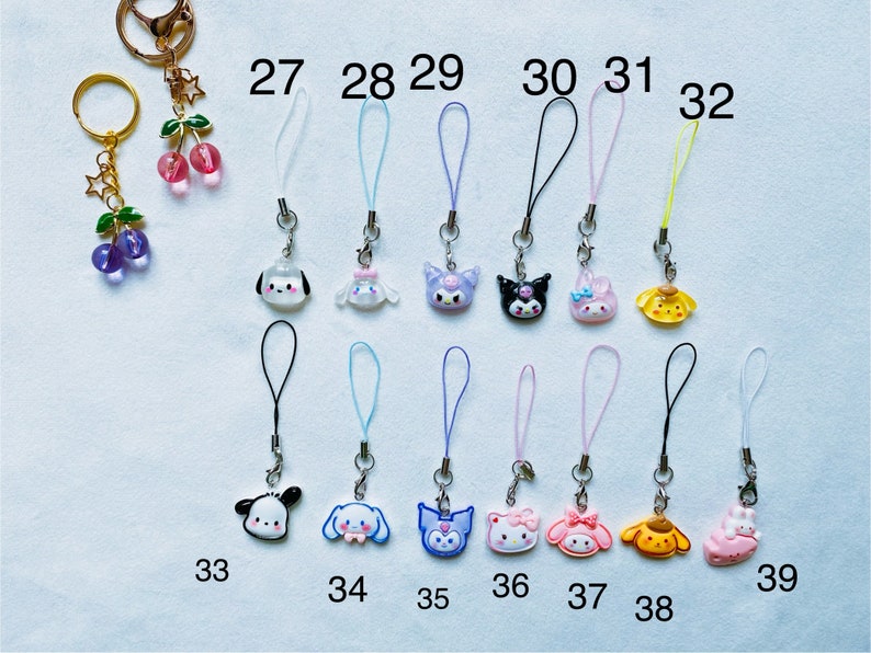 Pode incluir: Um conjunto de 12 pingentes de telefone coloridos com v&aacute;rios personagens de desenhos animados. Os pingentes s&atilde;o presos a cordas de diferentes cores, incluindo preto, branco, azul, rosa e amarelo. Os pingentes s&atilde;o numerados de 27 a 39.
