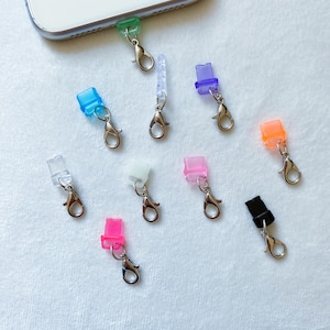 May include: Assortment of colorful phone charms with a silver clasp. The charms are shaped like small squares and rectangles.
