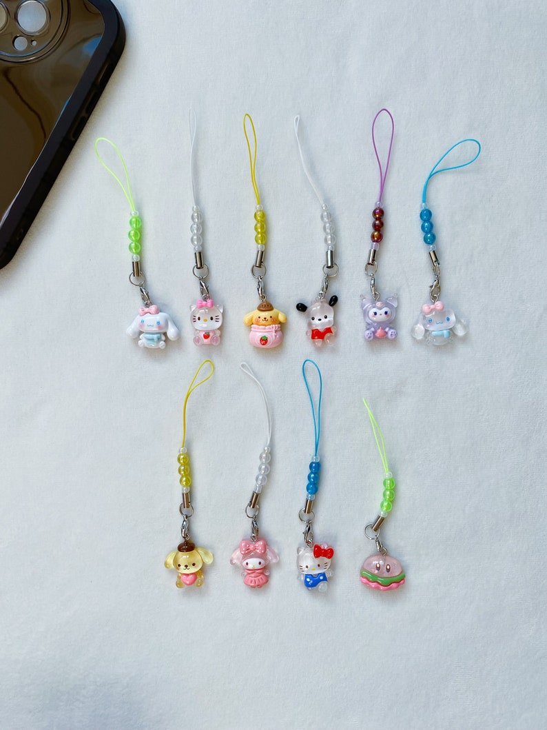 Pode incluir: Uma cole&ccedil;&atilde;o de 12 pingentes de telefone coloridos com personagens de desenhos animados populares. Os pingentes s&atilde;o feitos de pl&aacute;stico transparente e t&ecirc;m uma variedade de cores e designs. Cada pingente &eacute; preso a um cord&atilde;o com contas.