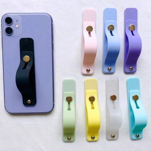 May include: A set of ten phone grips in various colors, including light blue, pink, yellow, green, and white. Each grip has a small gold button in the center.